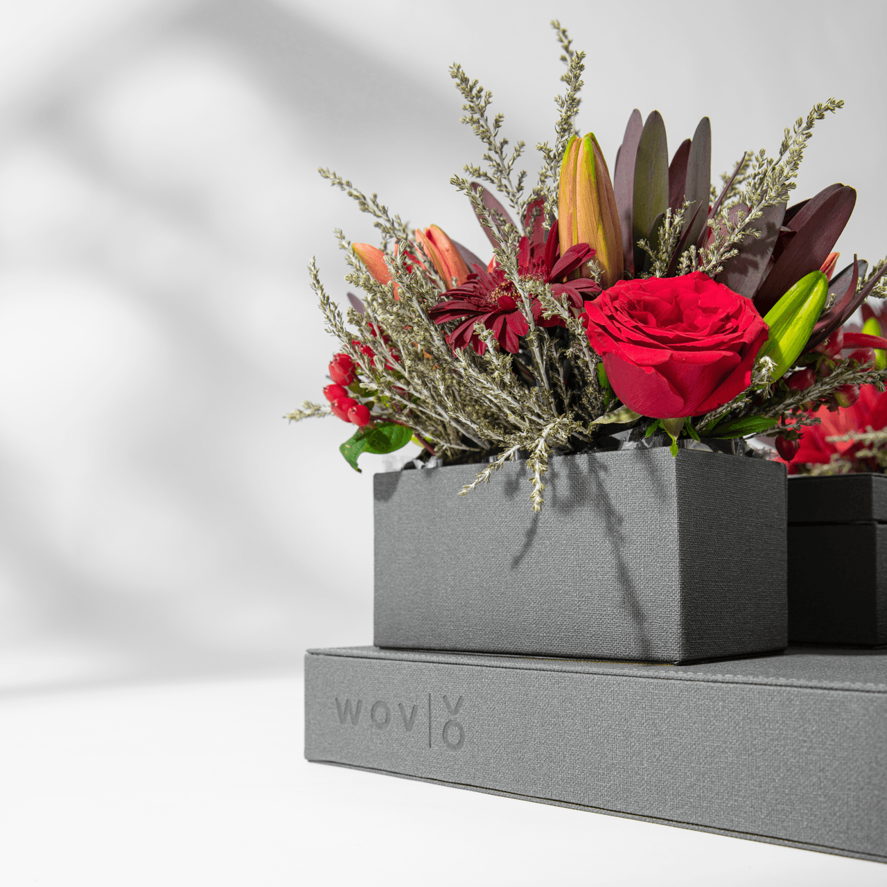 Close-up of a grey Vow presentation box with rich red roses and dark florals against a white background